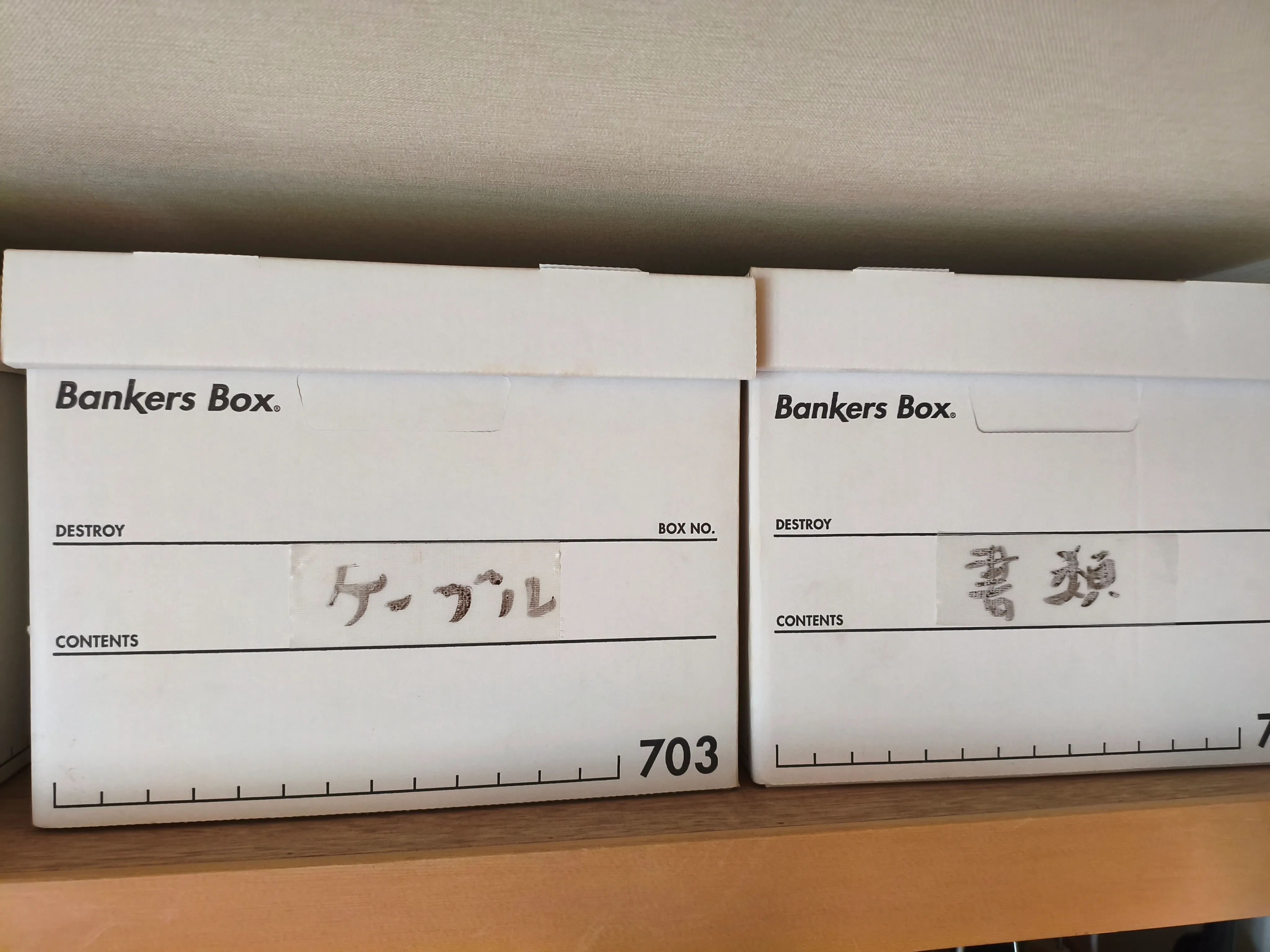 白いバンカーズボックスの側面に、マスキングテープで「ケーブル」「書類」と手書きしたラベルを貼っている